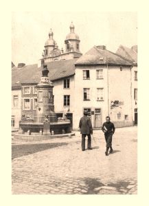 À nouveau, cette photo nous permet de découvrir des façades et des alignements de toitures disparus et qui, de surcroît, ne sont connus par aucun autre document. Le café visible derrière les personnages appartient en 1912 à Louis Lothaire (« Zoulou ») et deviendra le Café de la Jeunesse, aujourd'hui le Rimbaud.