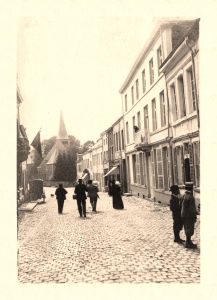 Vue d’ensemble : à droite, l’étude du notaire Fernand Dassonville, identifiable par le balcon en fer forgé. En face, la maison du Dr Jean Simon avec un garde-corps en fonte de type Nestor Martin. Au-delà, l’arvô, passage couvert menant à la rue de la Teinture. La rue Saint-Gilles, comme la place du Marché, a subi un incendie le 27 octobre 1938, détruisant cinq maisons du côté droit.